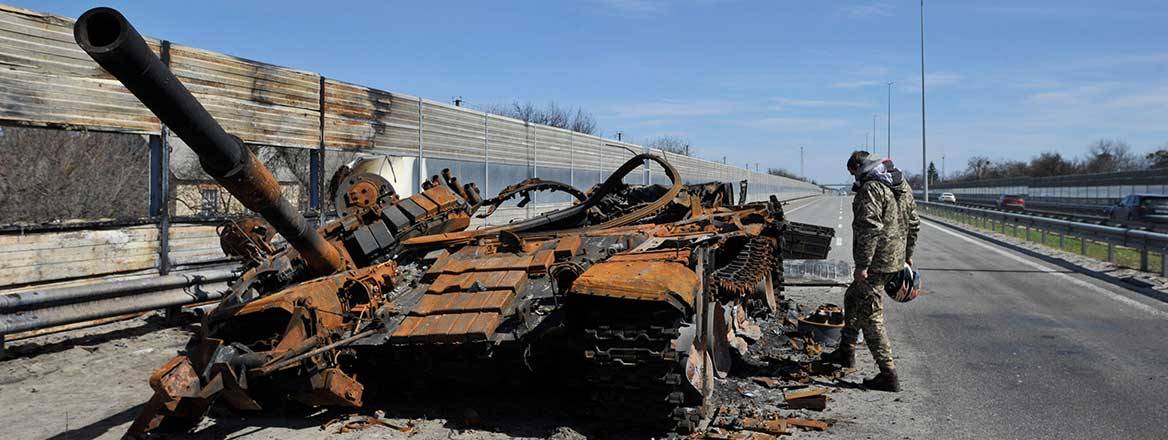 A destroyed Russian tank on a major road with a person investigating next to it.