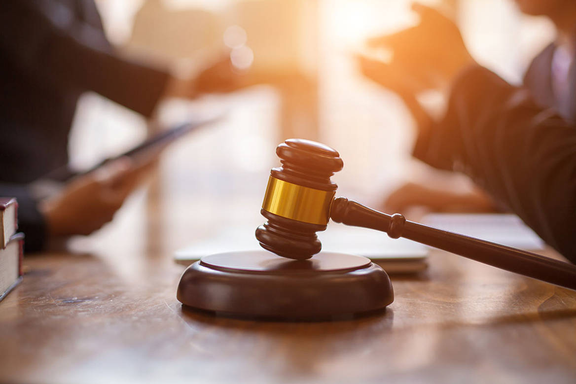 A gavel sits in the centre of the frame with the hands of two people behind it facing each other