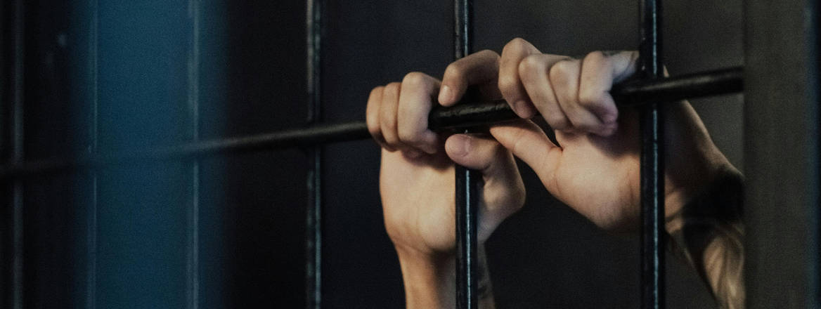 Hands of a person holding onto metal railings in a jail