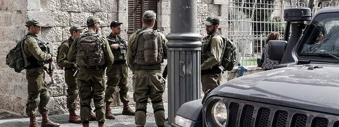 Group of soldiers standing at the side of a street with the front portion of a car in the foreground