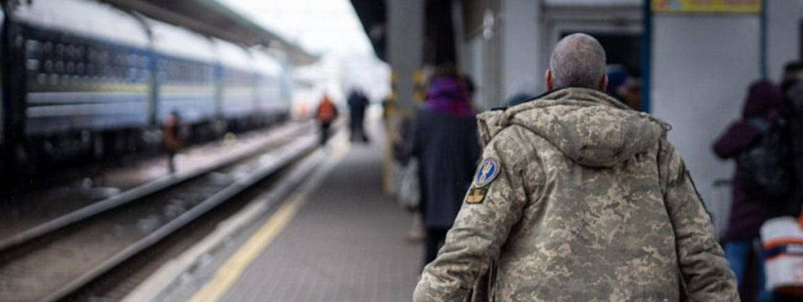 Uniformed soldier walking away from the camera on a train platform.