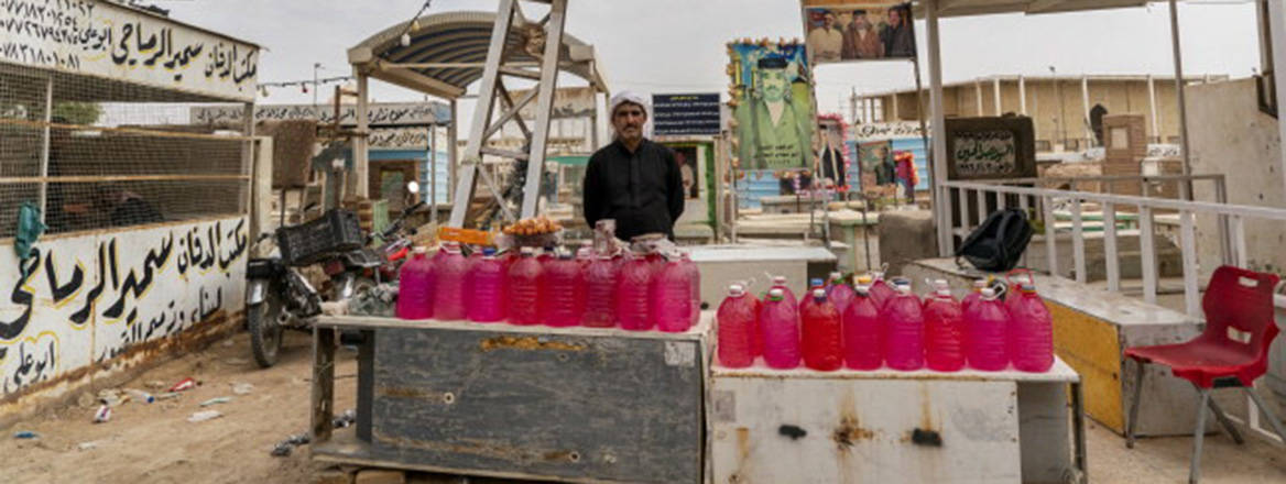 A man in a small outside stall with water bottles in front.