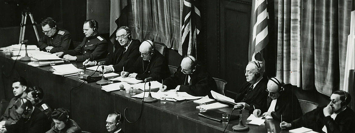 Black and white photograph of a number of judges sitting at a courtroom bench in front of the flags of the United States, United Kingdom and Soviet Union