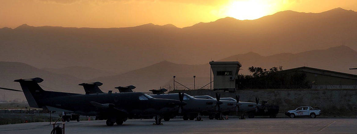 Aircraft and airport infrastructure in the foreground; sun setting over mountains in the background