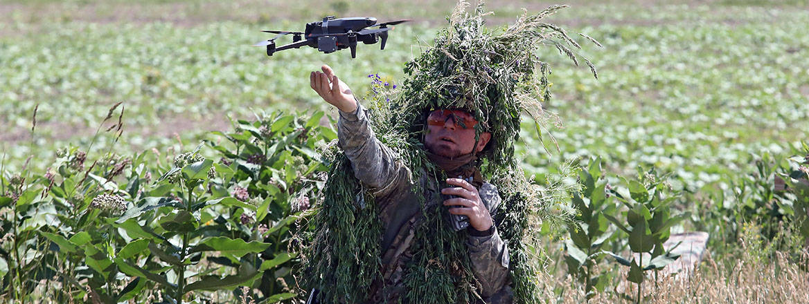 military pilot in camouflage holding a small UAV