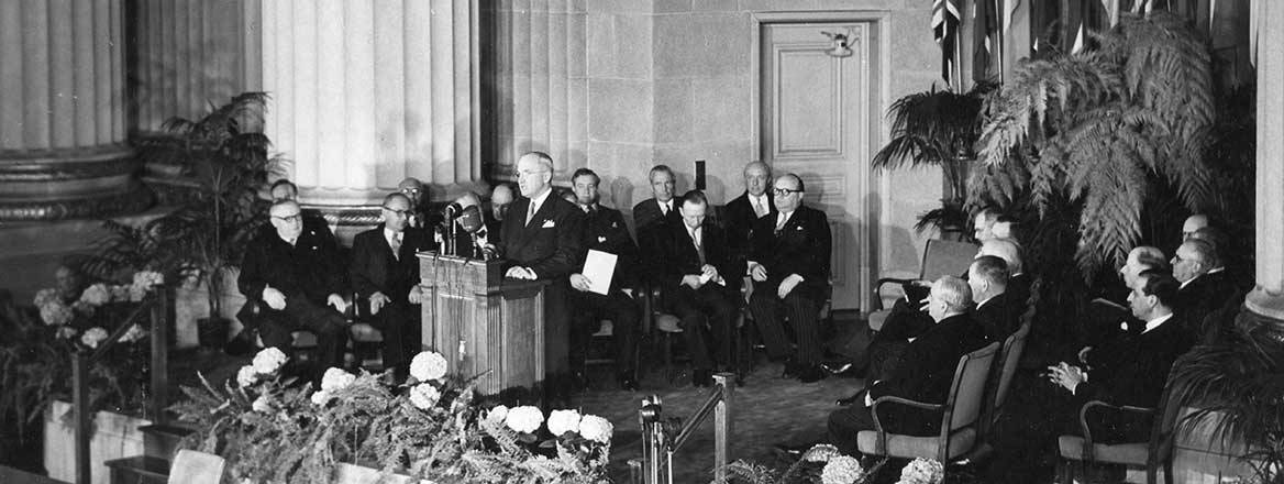 Harry Truman at a lectern addressing various representatives.