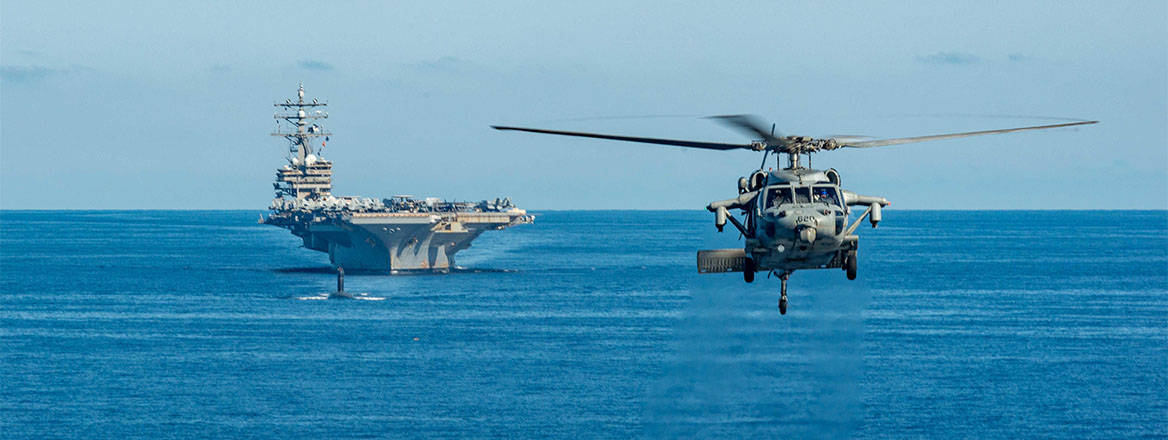 A US Navy MH-60S Sea Hawk flies in front of a formation with the Nimitz-class, nuclear-powered super-carrier, USS Ronald Reagan and a Los Angeles-class fast-attack submarine with Submarine Group Seven during joint training operations with the South Korean Navy in the East Sea, September 30, 2022 near Busan, South Korea