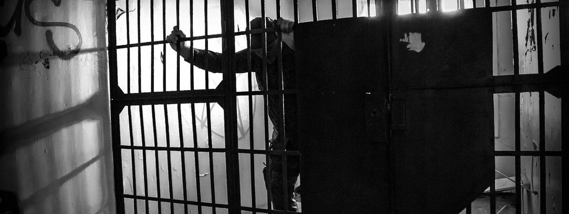 A prisoner leans against the bars of a prison cell