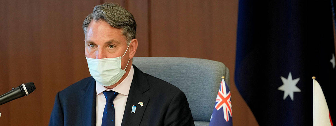 Richard Marles wearing a mask and sitting on a chair with a small Australian flag, and a toy koala, on the table