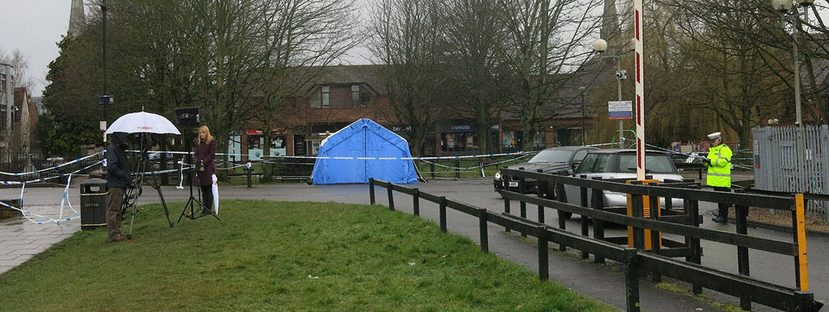 A news reporter being interviewed in front of a blue forensic investigation tent.