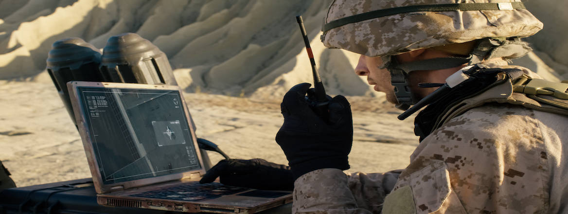 A soldier uses a laptop to track a target during a military operation in the desert