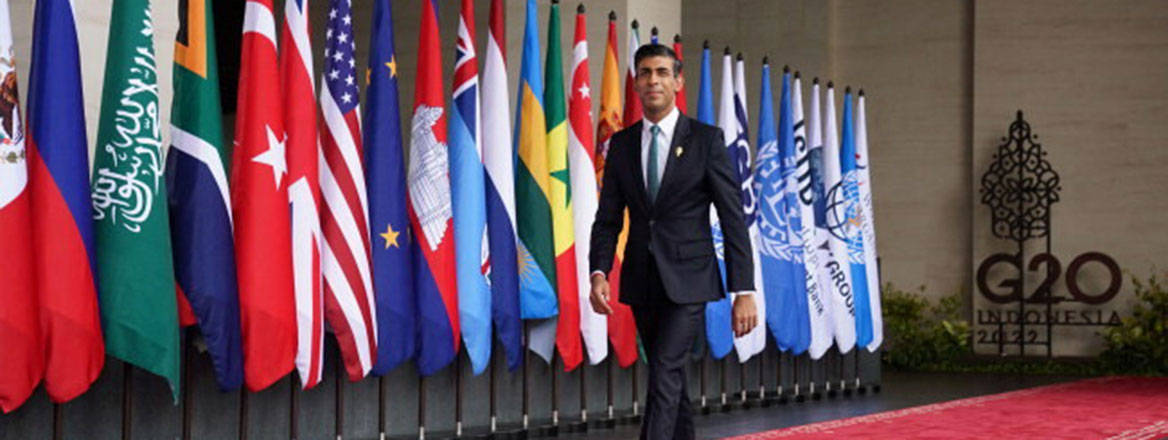 Rishi Sunak walking on a red carpet with many flags of the G20 nations behind him