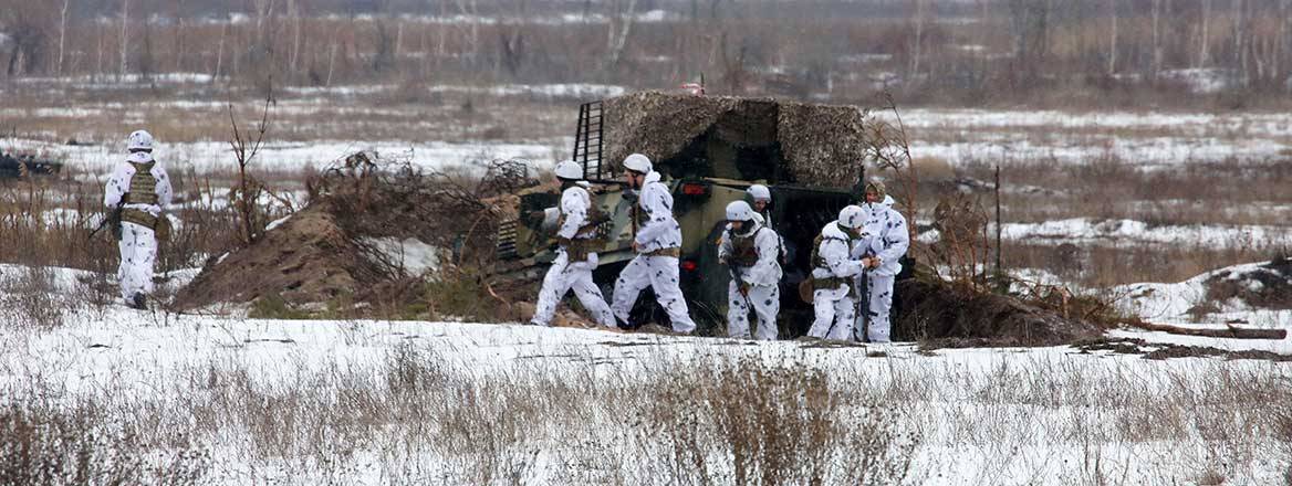 Several Ukrainian armed forces personnel in white camouflage standing near a military vehicle on snowy and icy ground