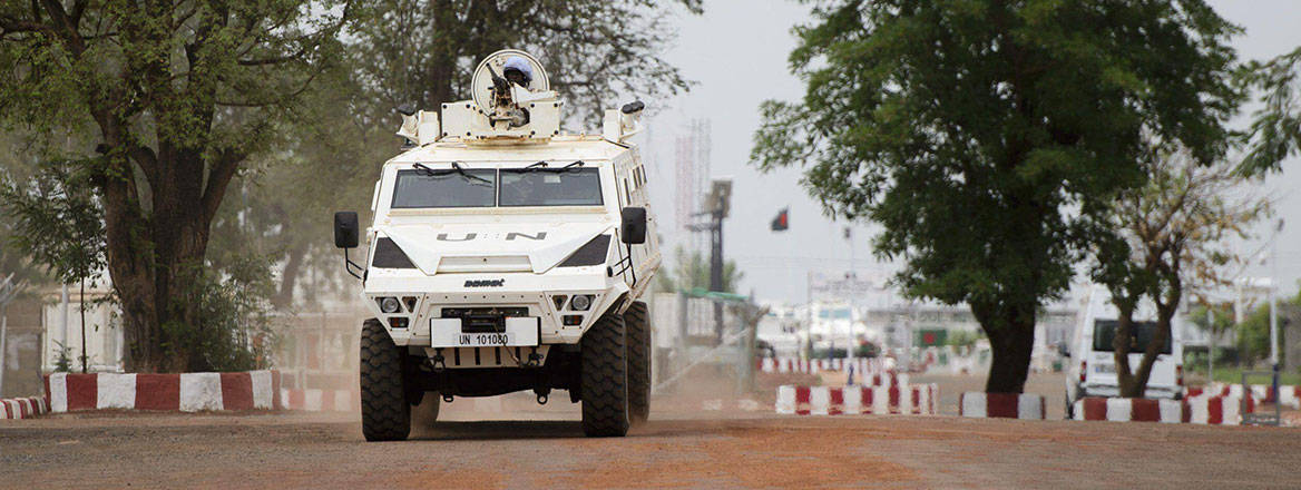 A UN vehicle facing the camera driving on a rough road with some trees in the background