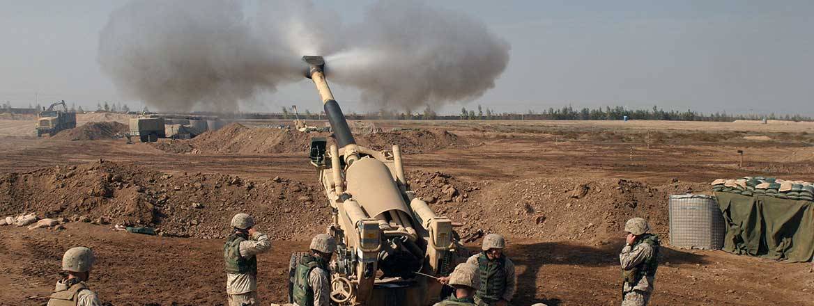 US Marines surrounding an artillery piece shortly after firing. The terrain is in open country with brown earth.