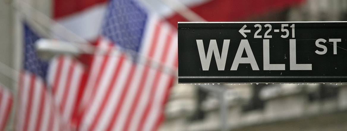 Wall Street sign in front of a building decorated with US flags