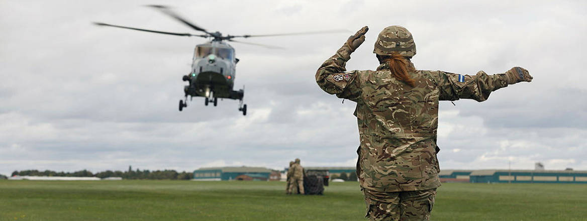 A female Air Trooper, part of HQ Sqn, 6 AAC marshalling a Wildcat Helicopter