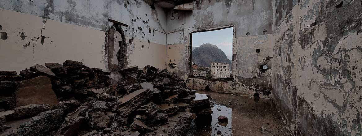 The damaged inside of a building with the view from a window on the far side of the room.