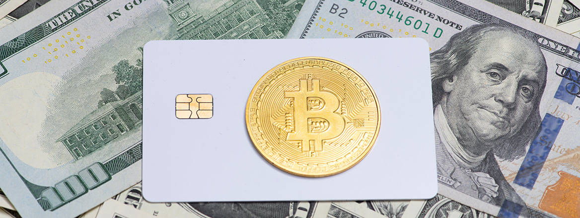 Conceptual image of a credit card with the Bitcoin symbol, laid on a bed of US banknotes.