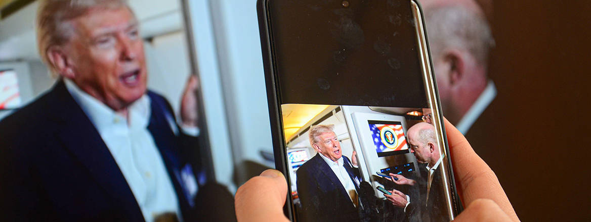 A camera-phone is seen capturing an image of a television screen that displays US President Trump answering questions to to members of the press aboard Air Force One. 