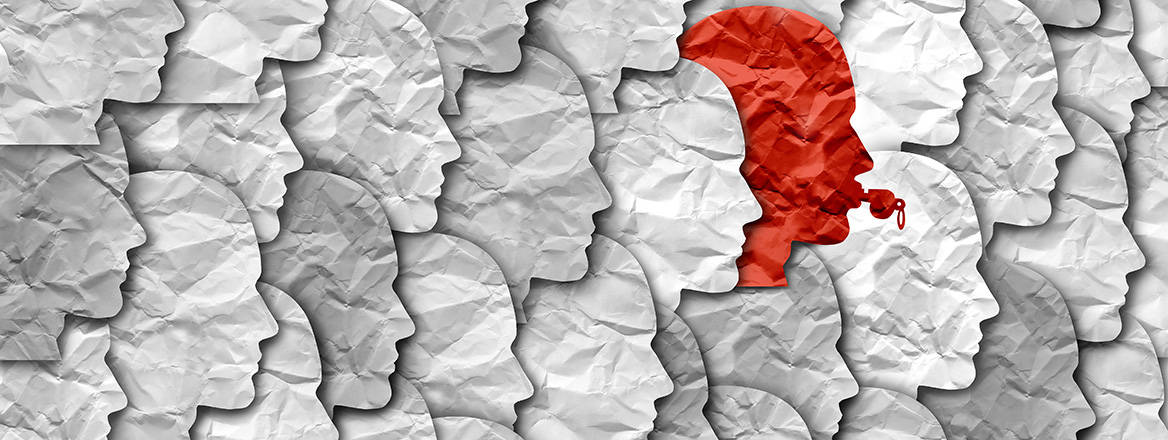 Stock image of layers of facial silhouettes cut from crumpled off-white paper, laid out like the scales of a fish. One silhouette amongst many is cut from red paper, and in its lips is the outline of a whistle.
