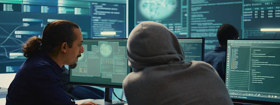A concept image of two people working at a computer, one in uniform and the other in a hooded sweater.
