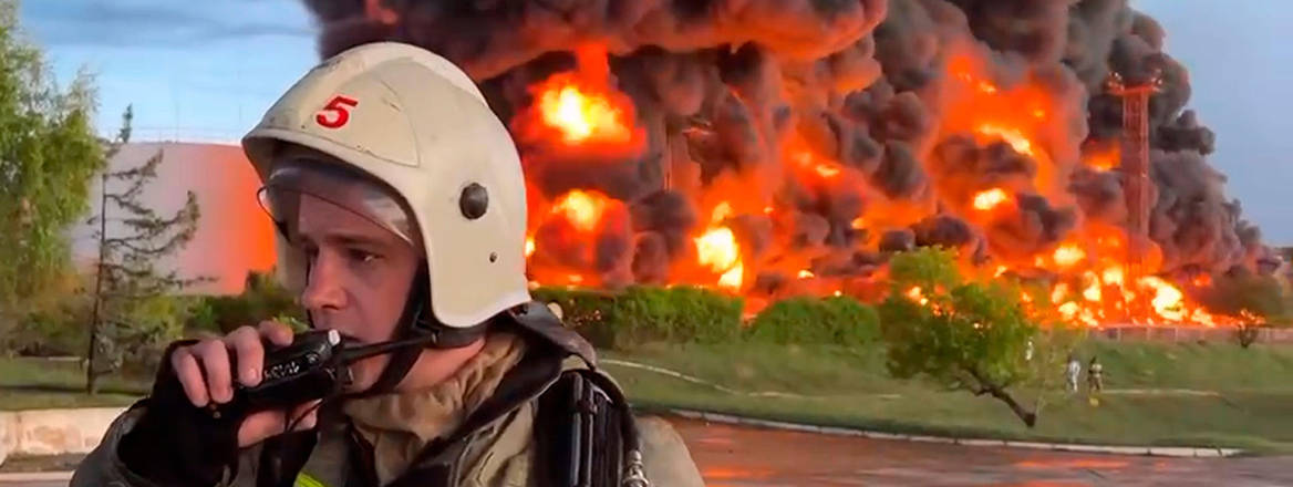 A firefighter speaks on the walkie-talkie as smoke and flame rise from a burning fuel tank in Sevastopol, Crimea. A massive fire erupted at an oil reservoir there after it was hit by a drone.