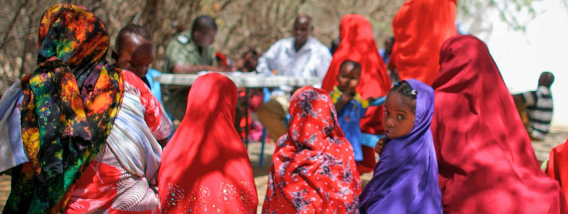 Women, children and men sitting in a group as part of the Deris Wanaag project