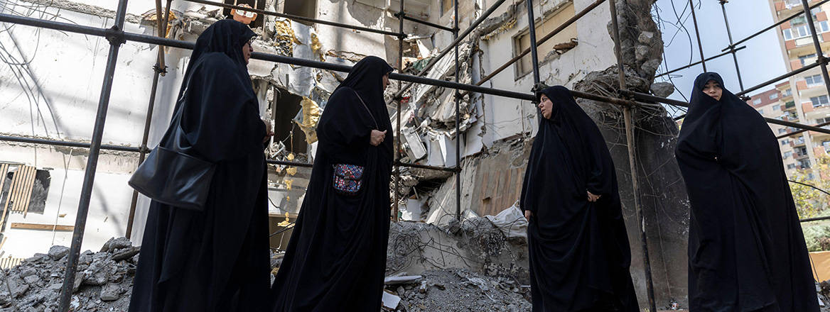 Iranian women walk past a destroyed housing compound targeted during the 12-Day War, 19 July 2025. Courtesy of Sipa US / Alamy