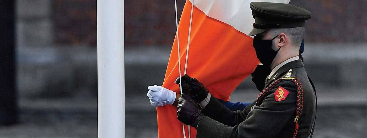 Member of the Irish defence forces wearing a face covering hoists the Irish flag
