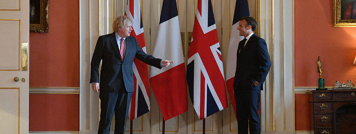 Boris Johnson and Emmanuel Macron facing each other in front of national flags.