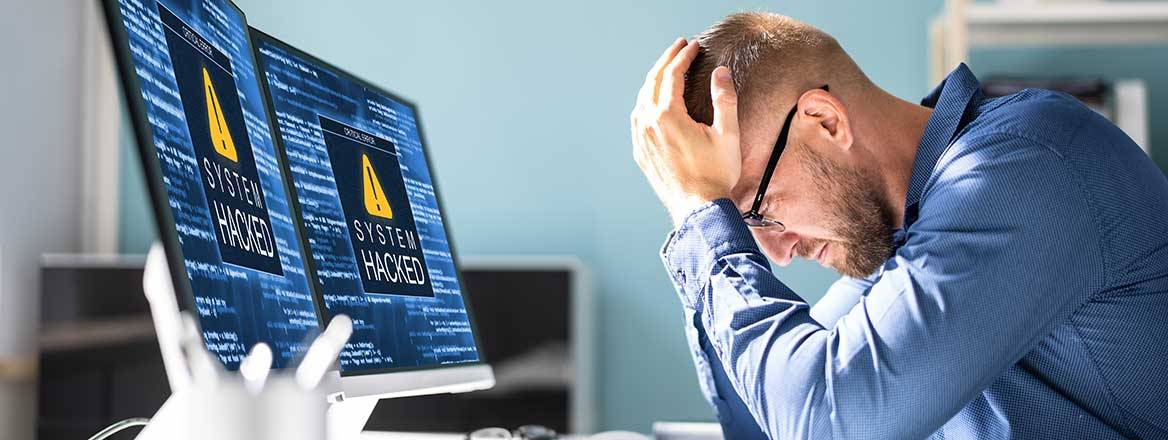 Man in front of computers suffering ransomware attack in an article on UK ransomware policy on 