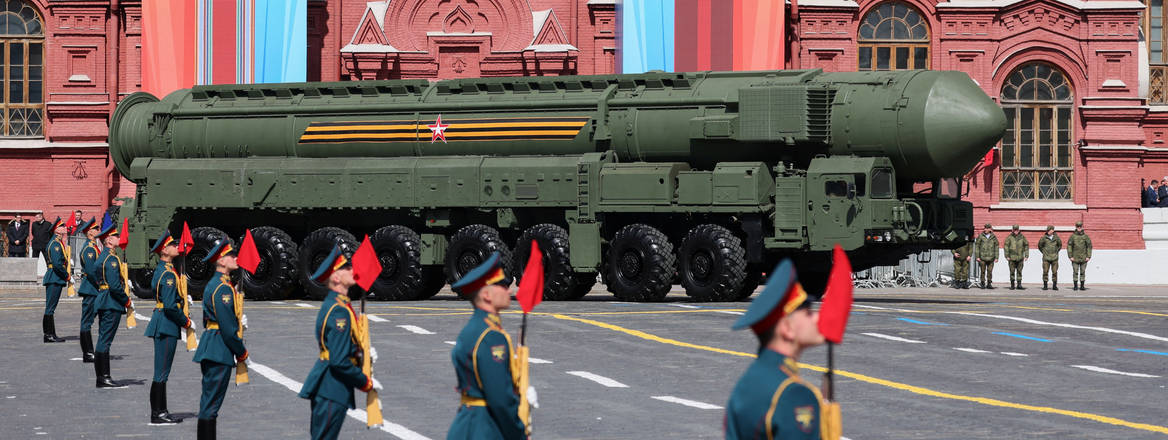Uniformed men stand in the foreground with a nuclear weapon on a tank behind them in front of the Kremlin, Moscow