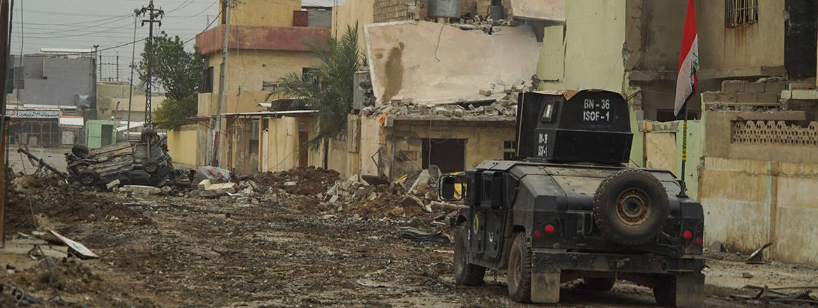 An Iraqi military vehicle on a street with rubble and destroyed buildings on the side of the road.  Courtesy of Mstyslav Chernov / Wikimedia / CC BY-SA 4.0