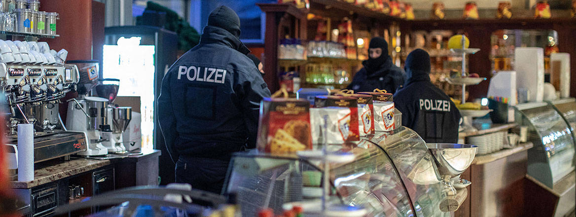 Policemen in an ice cream parlour in downtown Duisburg, Germany, as part of a raid on members of ’ndrangheta, December 2018. Courtesy of dpa picture alliance/Alamy.