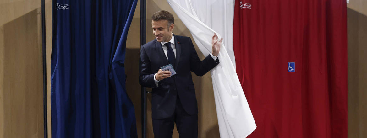 Shifting power: Macron will now have to negotiate with his government any proposal which requires resources or legislation. Image: Associated Press / Alamy Stock Photoel Macron leaves a voting booth draped in red white and blue curtains