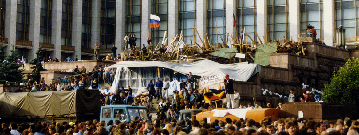 A barricade with many people in front of a building with a Russian flag centred and up high