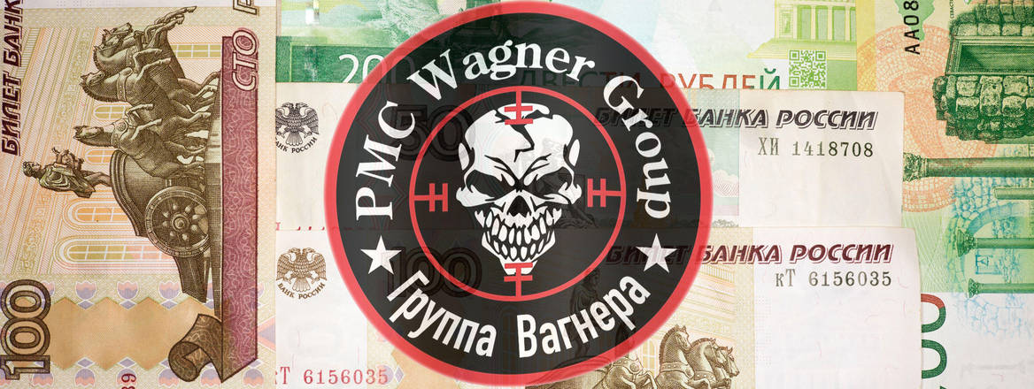Wagner Group's logo on a black background with the words Wagner Group in English and Russian Cyrillic and 100 and 200 rouble banknotes behind