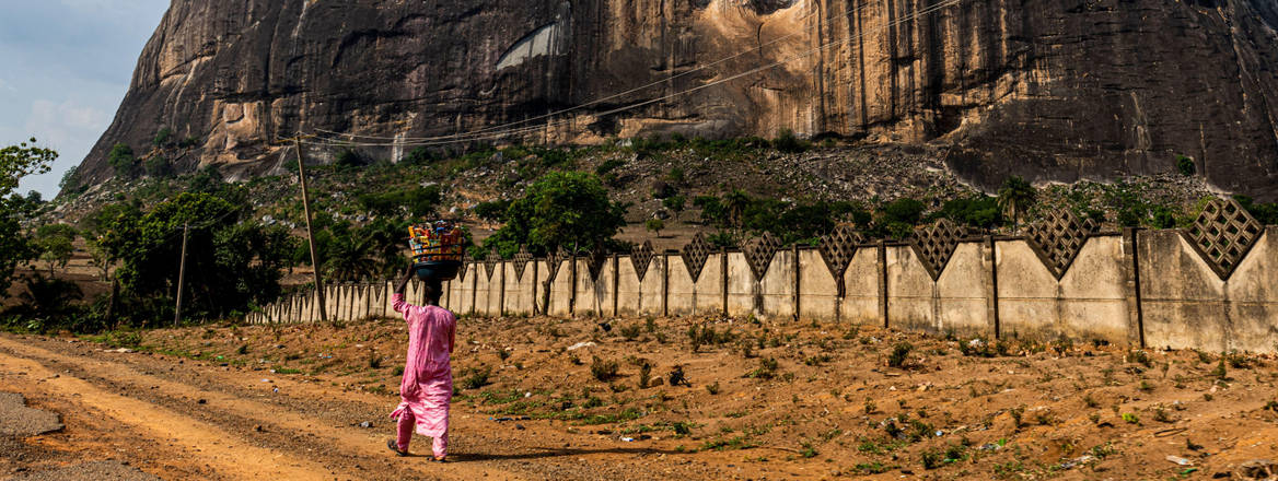 A woman walks in front of a rocky landscape, Nigeria