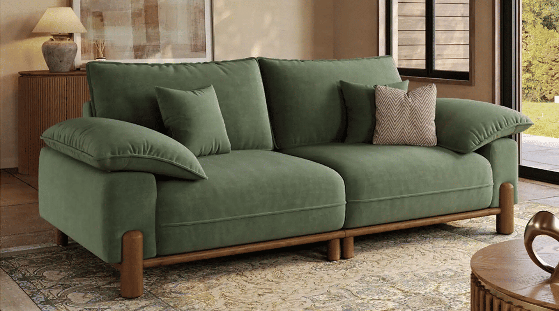 Green two-seater sofa with deep cushions and wide pillow-style armrests in a warm modern living room.