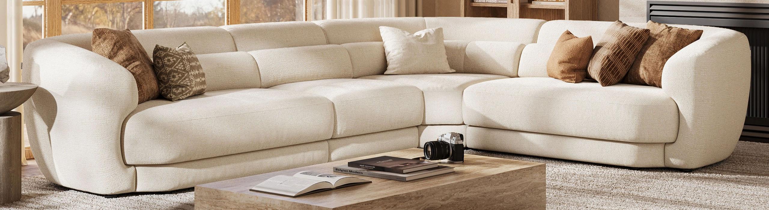 Cream low-back sectional sofa with curved arms and neutral throw pillows in a bright living room with a stone coffee table.