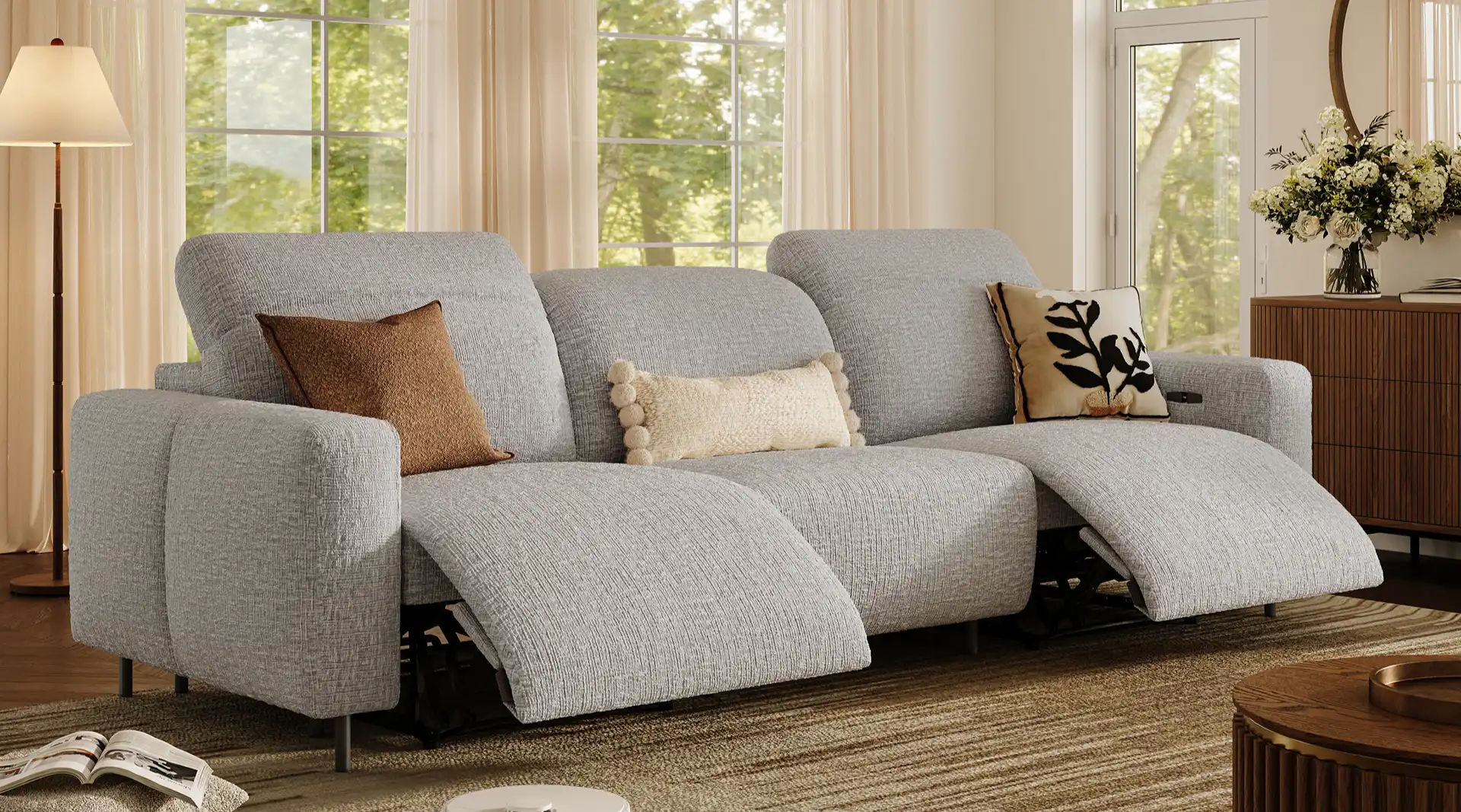 Light gray three-seater power reclining sofa with dual extended footrests and accent pillows in a bright modern living room.