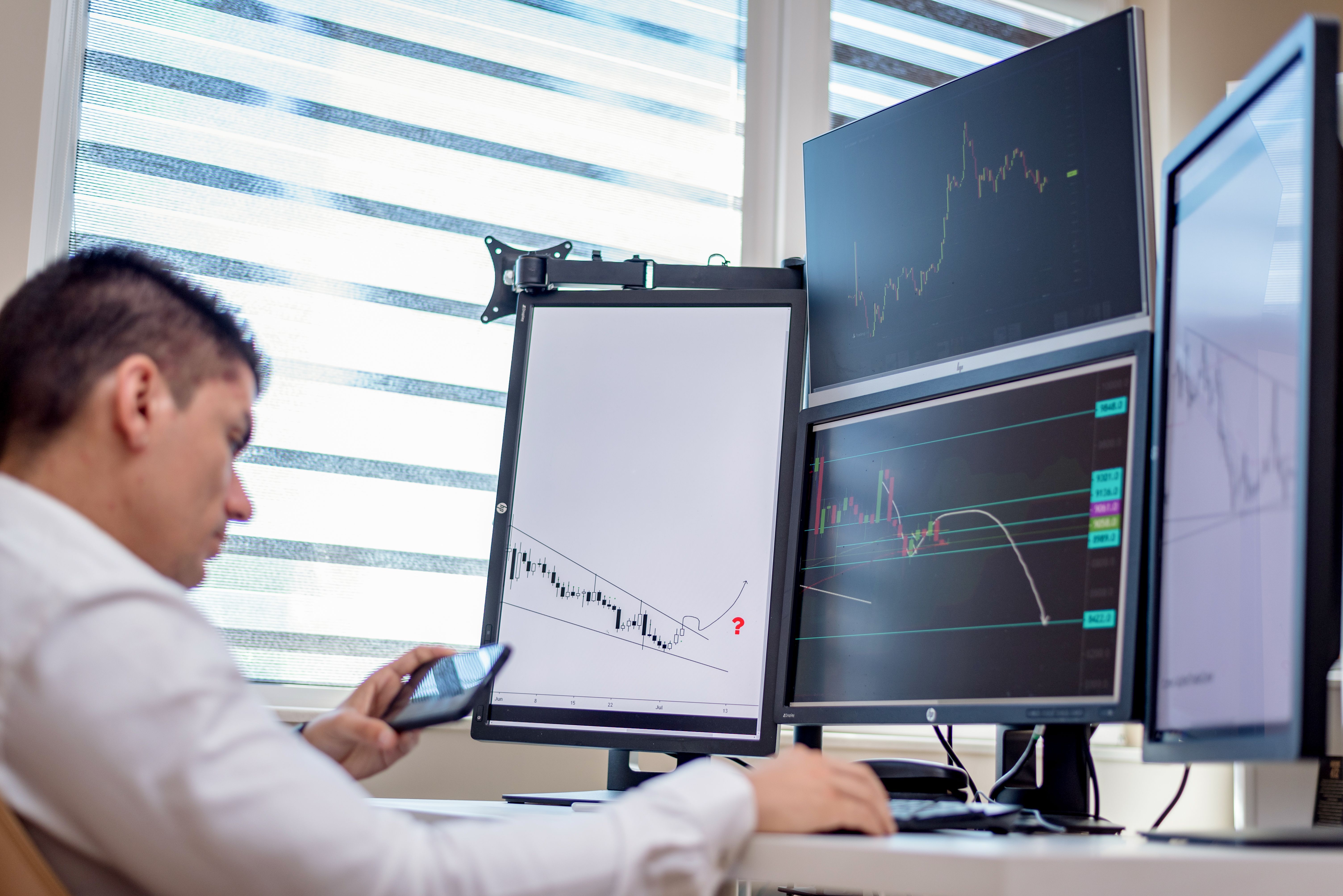 Financial trader analyzing stock market patterns and charts on multiple monitors