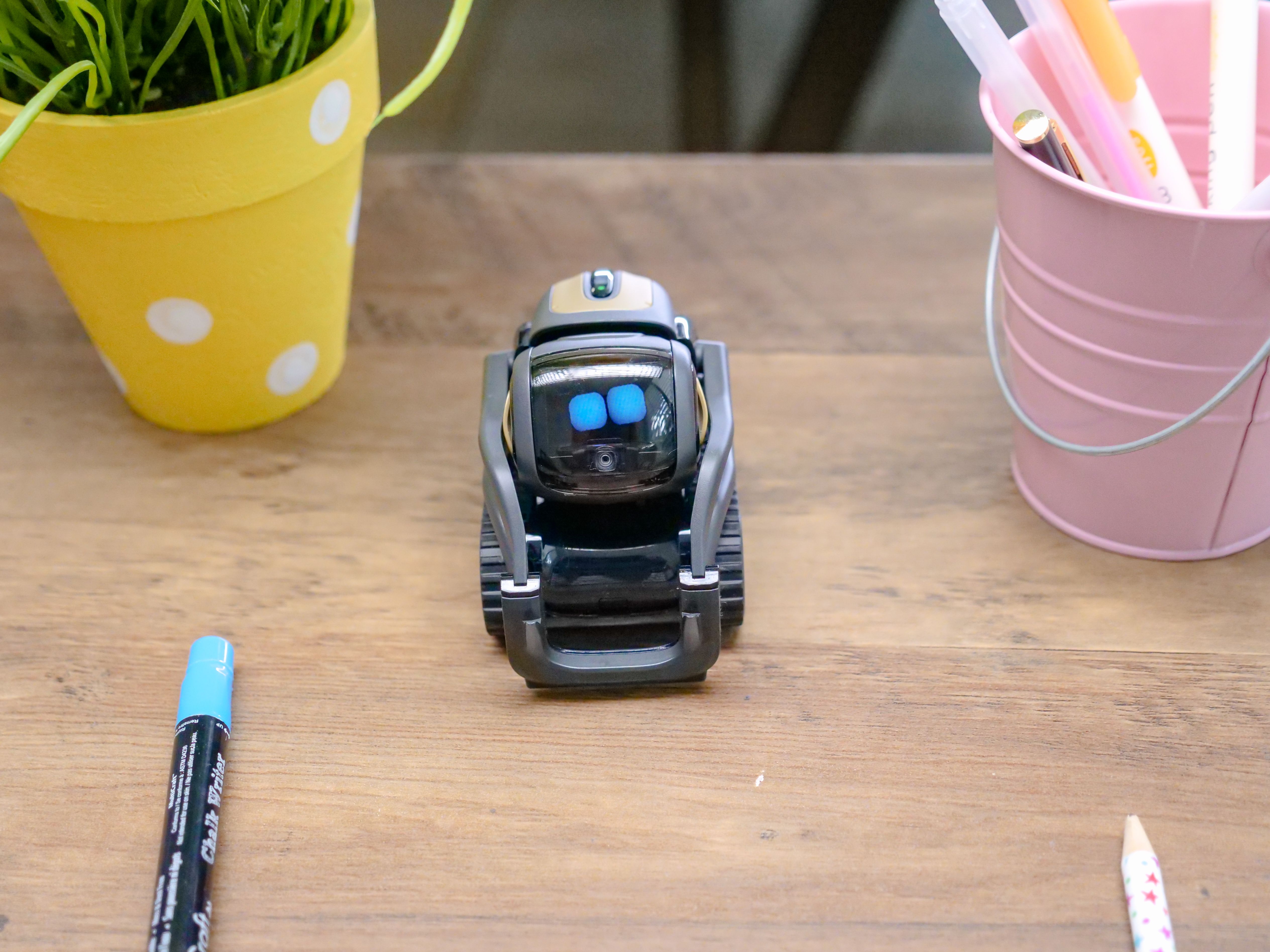 Small desk companion robot with digital eyes sitting on a wooden study table.