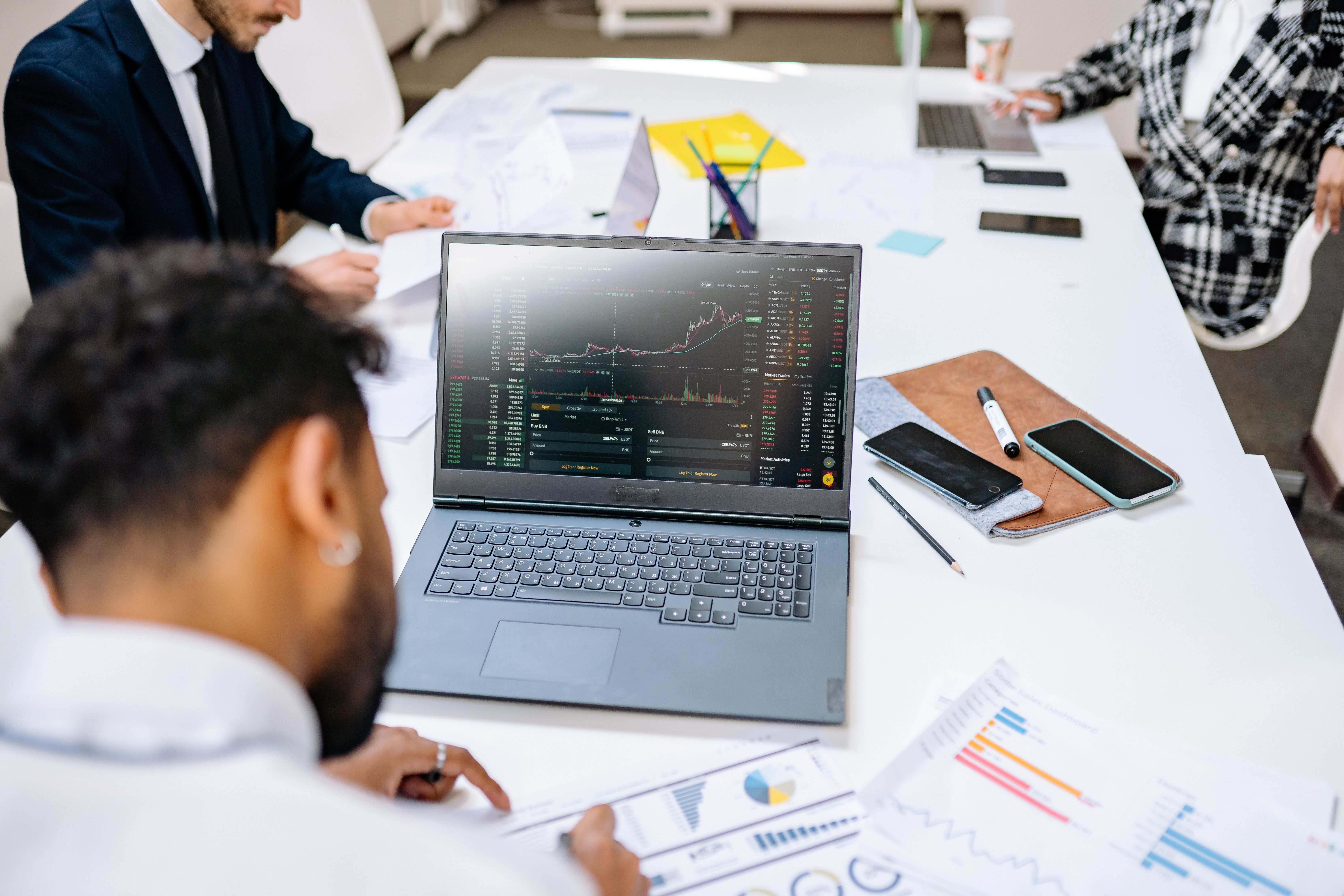 Financial analyst reviewing live stock market trading charts and performance reports in a corporate office meeting.