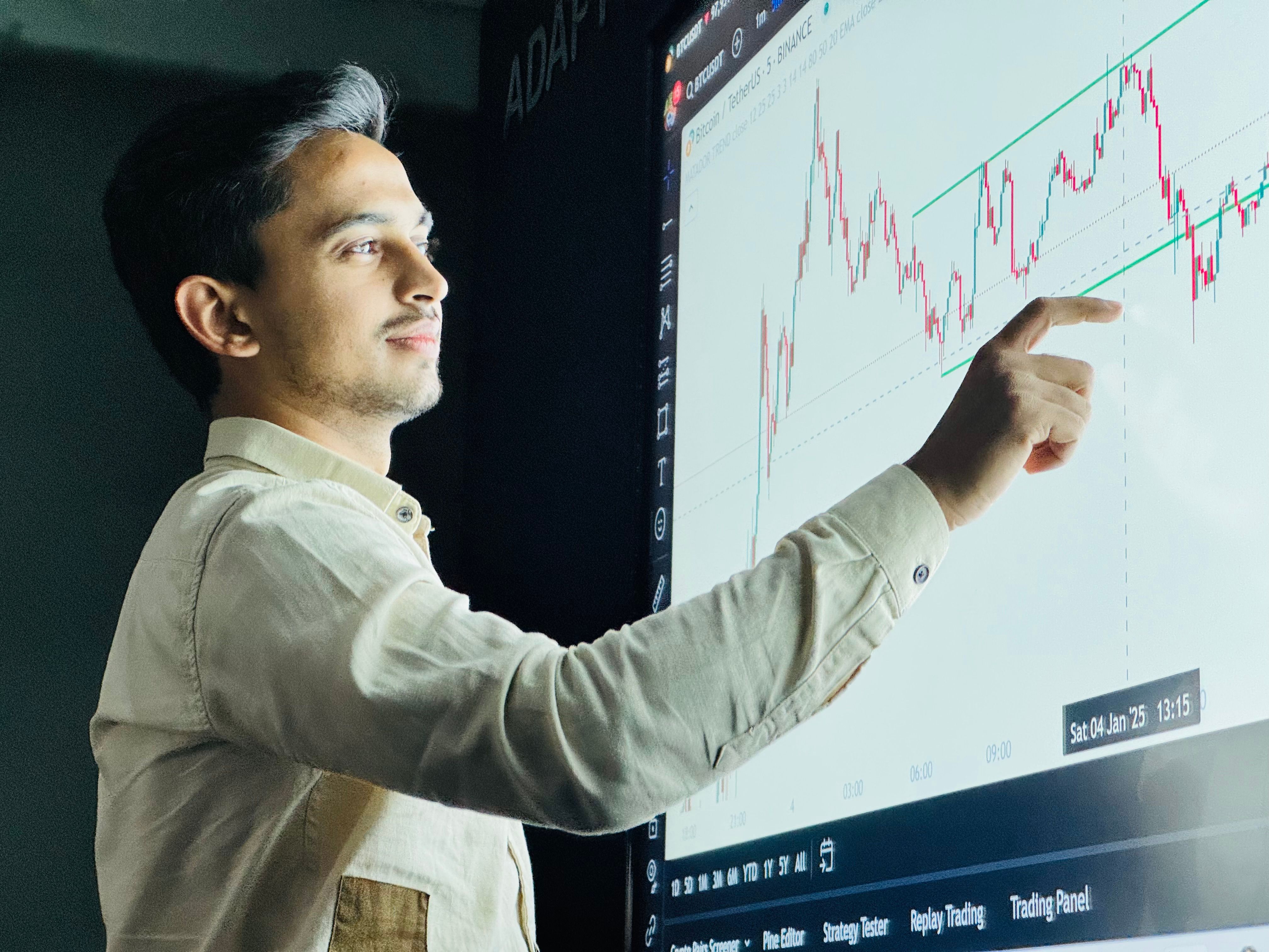 Young trader pointing at a stock trading candlestick chart on a large digital screen display.