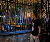 A person is gesturing enthusiastically while speaking to a group of smiling people casually seated on a brick ledge outdoors at night