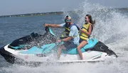 Two people are enjoying a thrilling ride on a jet ski, with water spraying around them.