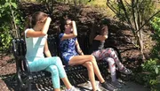 Three children are sitting on a bench with their hands over their eyes, as if shielding from the sun or playing a game.