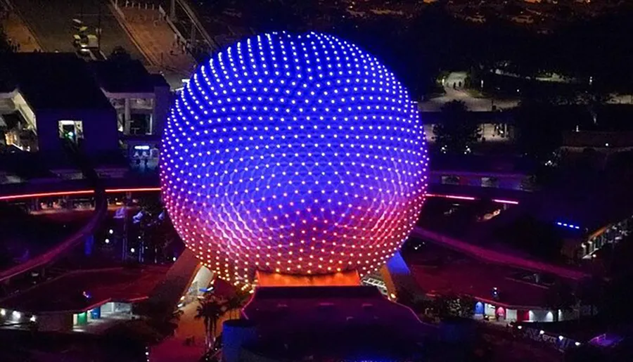 A nighttime aerial photo captures the illuminated geodesic sphere of Spaceship Earth, the iconic attraction at Epcot in Walt Disney World.